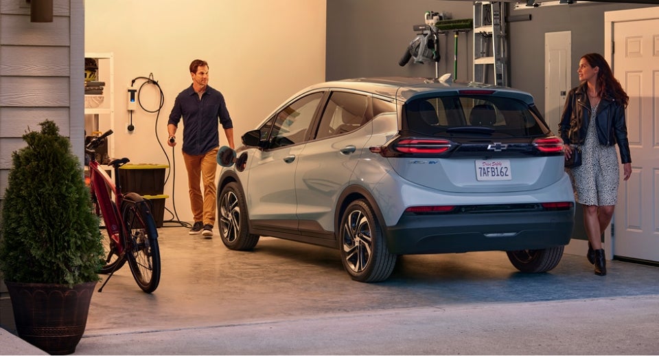 A Couple In Their Garage With the Man Plugging in the Charger for Their Chevrolet Bolt EV